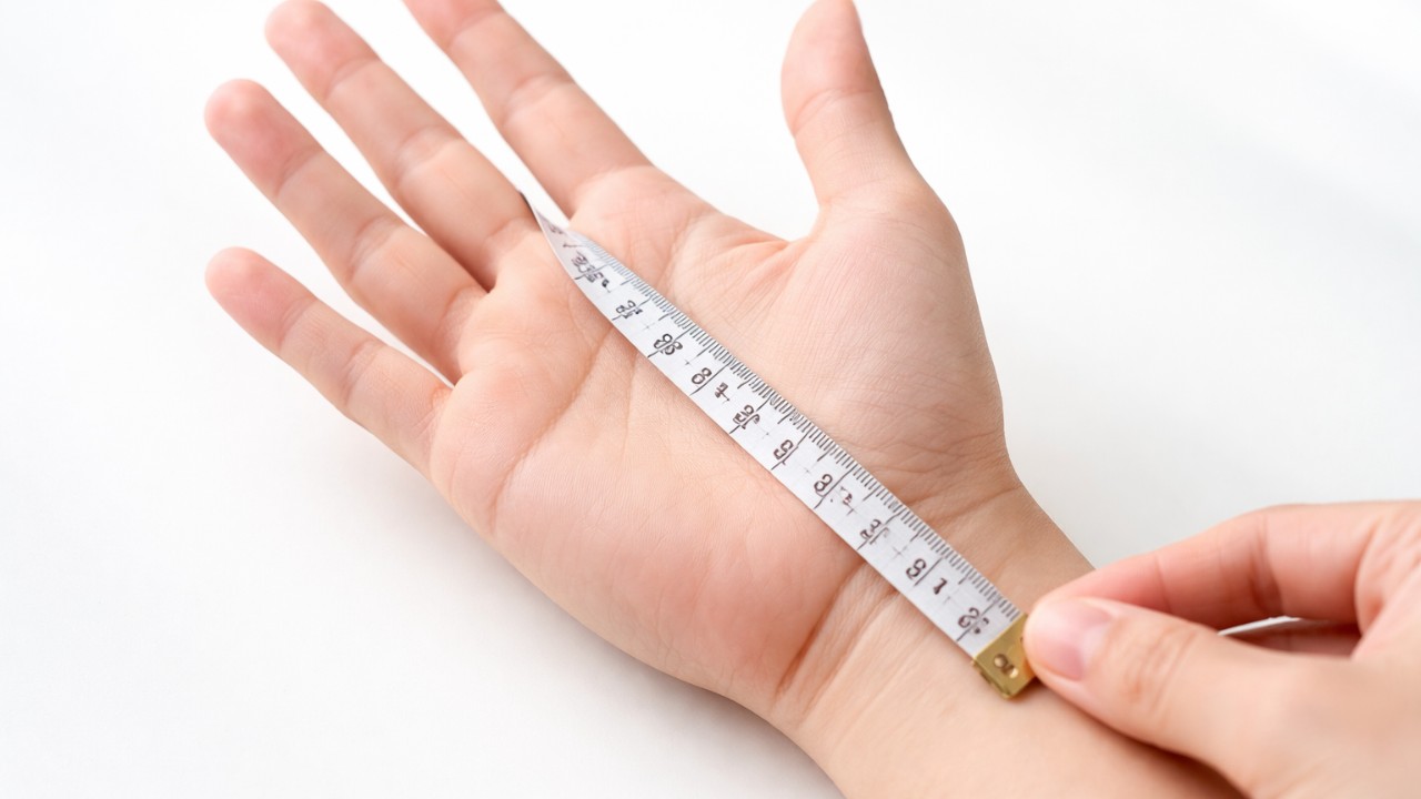 裁縫用メジャーで中指先から手首のしわまでを測る手元