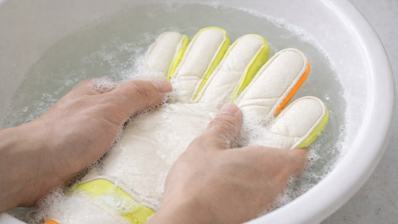 ぬるま湯の入った洗面器で、キーパーグローブのパームを指の腹でもみ洗いしている手元のアップ
