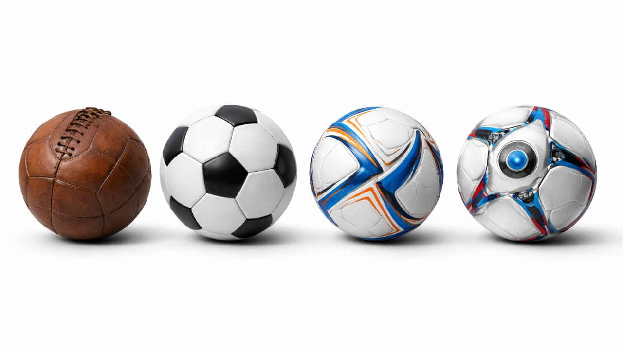 年代別に4種類のサッカーボールを横並び（革ひも付き、32枚パネル、近代熱圧着、センサー搭載イメージ）